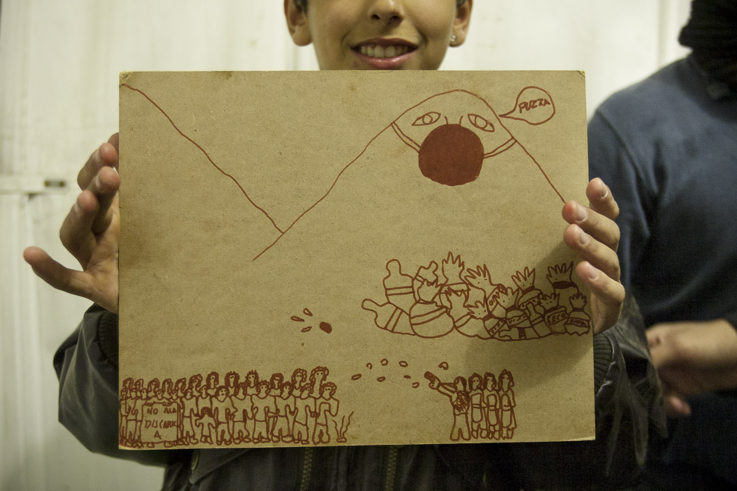 A young protester shows a drawing he made on a piece of carton during a night at the roadblock at Boscoreale's “roundabout”. Towering above the police shooting teargas at protesters, the mount Vesuvio wears a mask and laments the stench of the accumulated garbage.