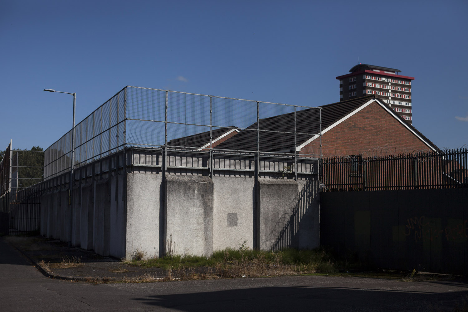 A “Peace Line” divides a Protestant area from a Catholic one in West Belfast. The points of contact between the two communities are known as “interfaces”, and are often the site of frictions and violence. Tall separation barriers known as Peace Lines mark some of these interfaces, with gates at the main connecting roads that are closed from sunset to dawn and are often operated by the local residents themselves.